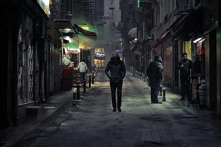 man in black hoodie walking beside concrete building at nighttime thumbnail