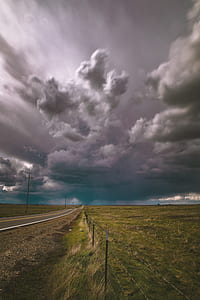 gray asphalt road surrounded by green grass under gray cloudy sky during daytime thumbnail