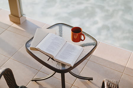 opened book near red ceramic mug above clear glass table thumbnail