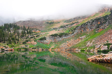 landscape photography of body of water beside mountain covered by fog thumbnail