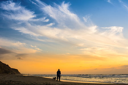 person standing on seashore under orange clouds and blue sky during sunset thumbnail