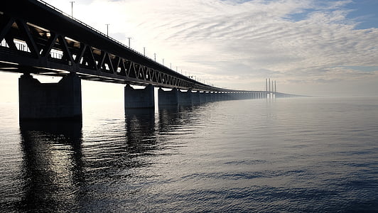 panoramic photography of bridge on body of water under gray clouds thumbnail