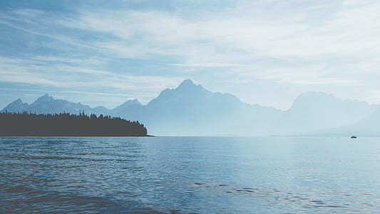 calm blue sea near mountains under grey sky thumbnail