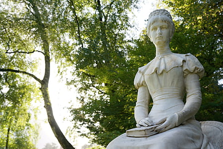 woman holding book statue under green trees thumbnail