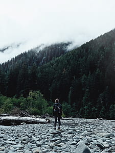 woman wears backpack stands in front of mountain with trees thumbnail