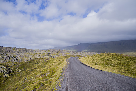 road between grass field under cloudy sky at daytime thumbnail