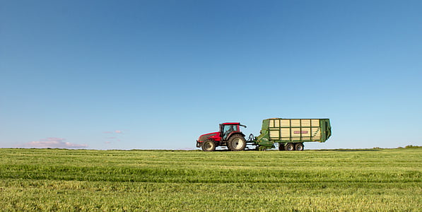 red tractor with green trailer on wide grass field thumbnail