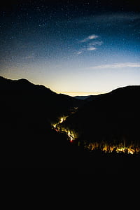 lighted road in the middle of mountain silhouette under blue sky at night thumbnail