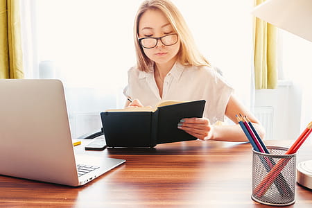 Young woman make notes in her diary. Laptop and pencils on a table in front of her thumbnail