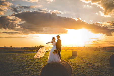 bride and groom taking picture on pale of hay under horizon thumbnail