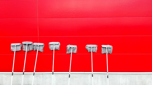 seven gray mops leaning at red wall thumbnail