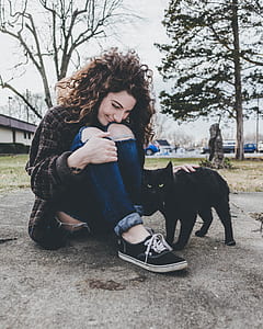 woman sitting on gray concrete pathway touching black bombay cat at daytime thumbnail