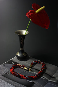 beaded red and black bracelet beside black and gold-colored vase and red anthurium flower in closeup photography thumbnail