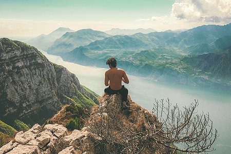 man on mountain cliff near body of water thumbnail