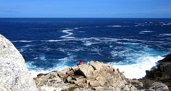 person wearing orange top on gray stone near body of water thumbnail