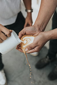 person pouring coffee latte on person's hands selective focus photography thumbnail
