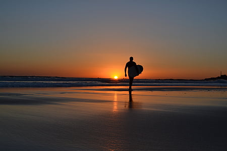 man carrying surfboard while walking of shore sand thumbnail
