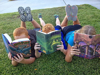 three childrens holding Harry Potter books while laying on grass photograph thumbnail