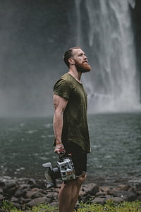 man holding gray camera beside waterfalls thumbnail