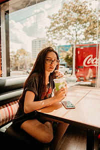 woman sitting on black chair near table holding disposable cup thumbnail