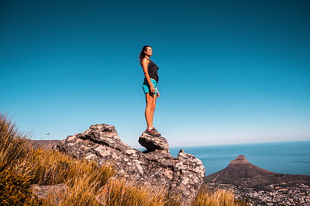 Woman in Black Top and Blue Shorts on Stone Under Blue Sky thumbnail