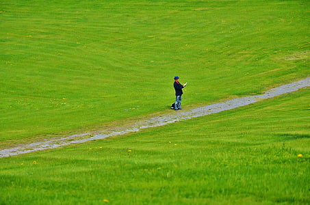 man standing on road in between grass field thumbnail