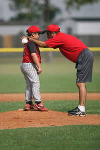 selective focus photo of man talking boy in baseball field during daytime thumbnail