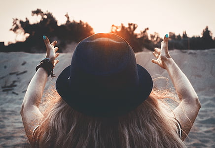 woman wearing a hat sitting on sand during dusk thumbnail