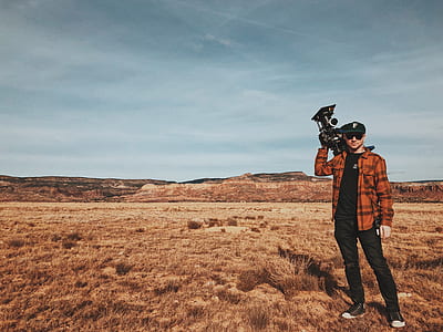 man standing on dried grass field while holding camera thumbnail