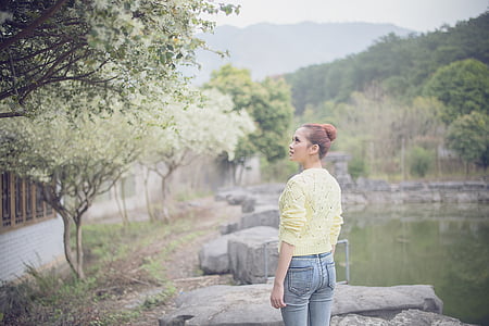 woman wearing green sweater standing beside body of water near tree thumbnail
