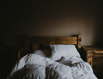 white bedding set and brown wooden bed frame with low light photo thumbnail