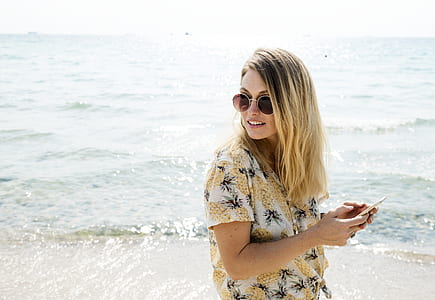woman in yellow and white shirt holding smartphone on seashore thumbnail