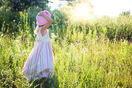 girl standing on green grass field while holding her pink hat during daytime thumbnail
