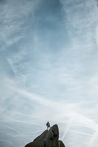 man standing on gray mountain cliff under cloudy sky thumbnail