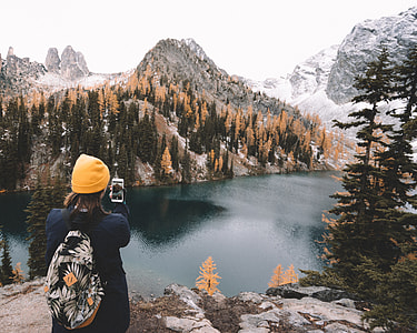 woman taking photo of lake near snow-covered mountain thumbnail