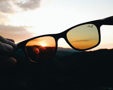 person's holding brown Ray-Ban Wayfarer sunglasses point sunset thumbnail