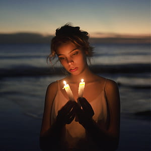 woman in white spaghetti strap top holding two white lighted candles thumbnail