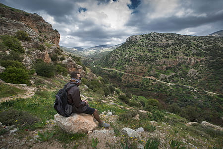 Man Sitting on Brown Boulder Top on Hill thumbnail