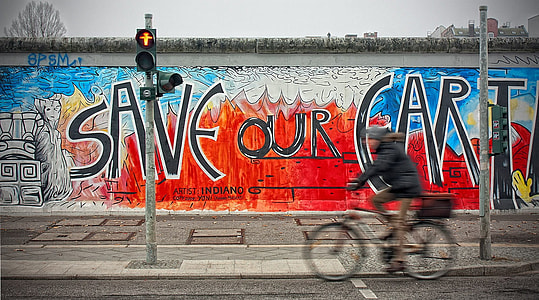 person riding bicycle on road near wall with Save Our Earth painting thumbnail