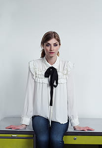 woman in white ruffled long-sleeved collared blouse and blue denim jeans sitting on green and gray stainless steel table thumbnail