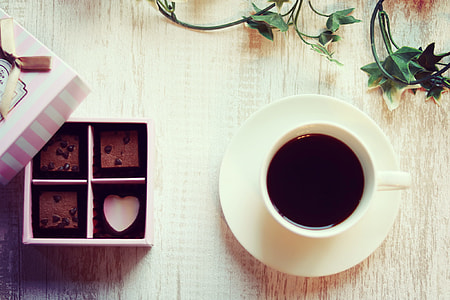 white ceramic cup with saucer and black coffee near chocolates thumbnail