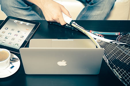 person holding white tennis racket beside MacBook thumbnail