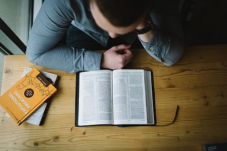 man sitting beside table reading book thumbnail