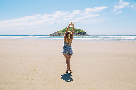 woman standing on white sand with hands above her head and islet with distance thumbnail