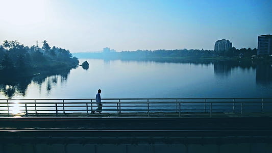 man walking on bridge between tress near highrise building thumbnail
