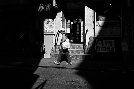 grayscale photo of man walking pass by store front thumbnail