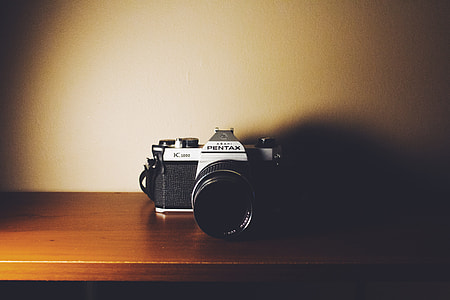 black Pentax DSLR camera on brown wooden shelf thumbnail