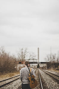 person holding guitar walking on train tracks thumbnail