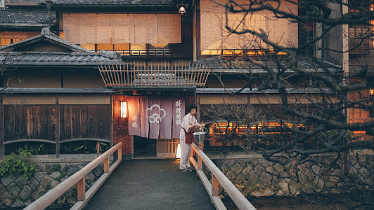 Japanese wooden house with woman in white clothes near river and bridge thumbnail