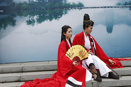 two women wearing dresses sitting in front of body of water thumbnail